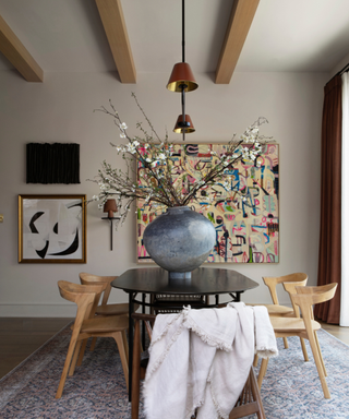 A taupe dining room with a large vase on a table and artwork on the walls.
