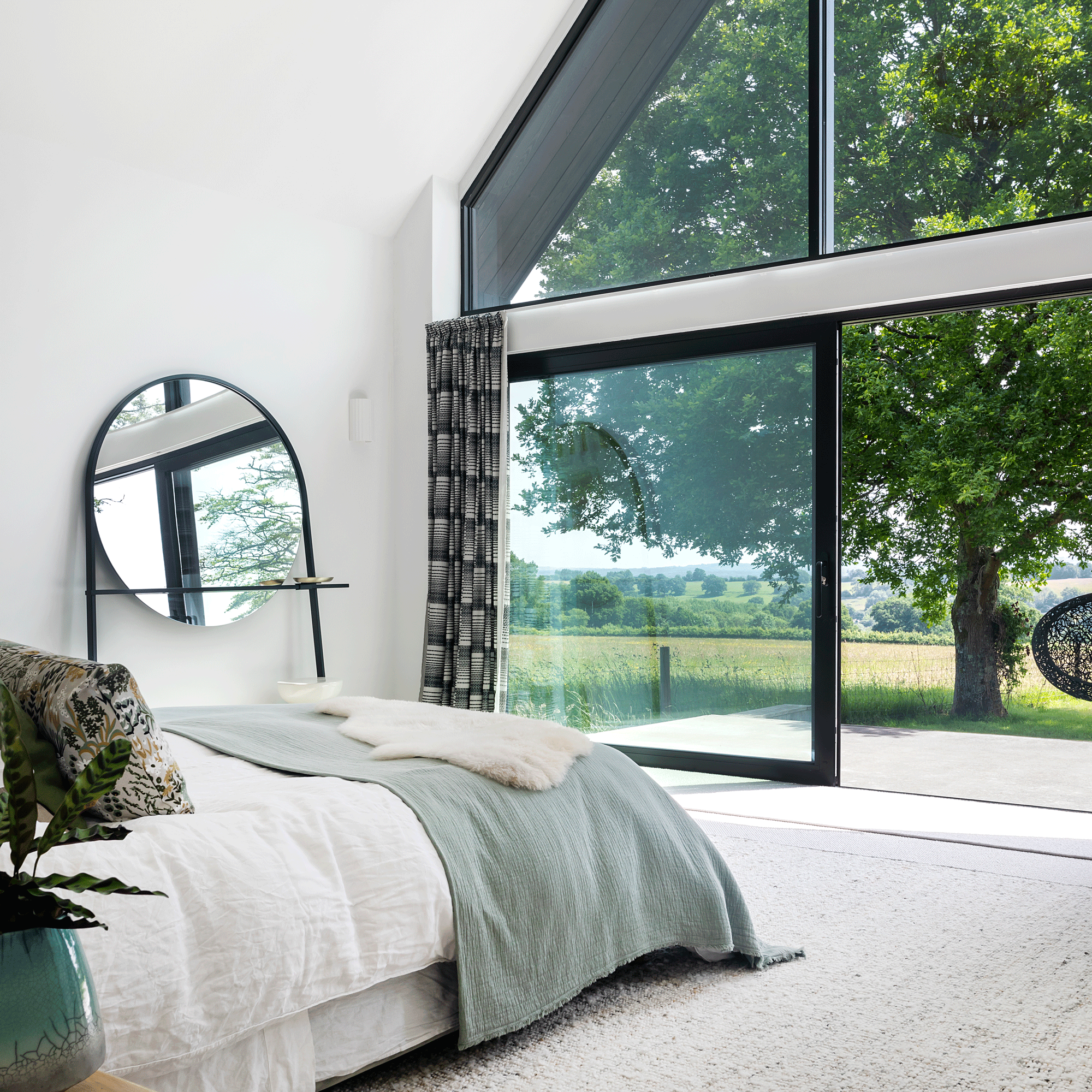 a bedroom with floor to ceiling vaulted glazing with a stunning countryside view