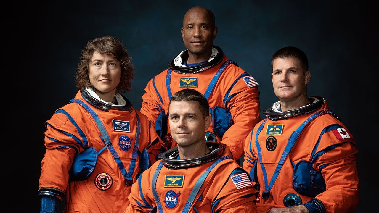 four astronauts in orange spacesuits pose for a portrait
