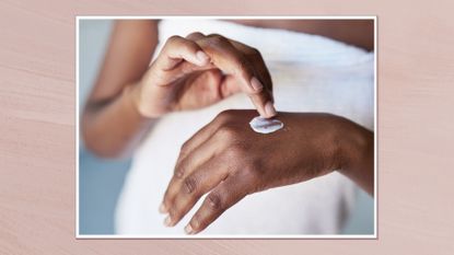 Close up image of woman&#039;s hands as she applies cream on the back of one of them, in a white frame against a dusky pink watercolour-style background