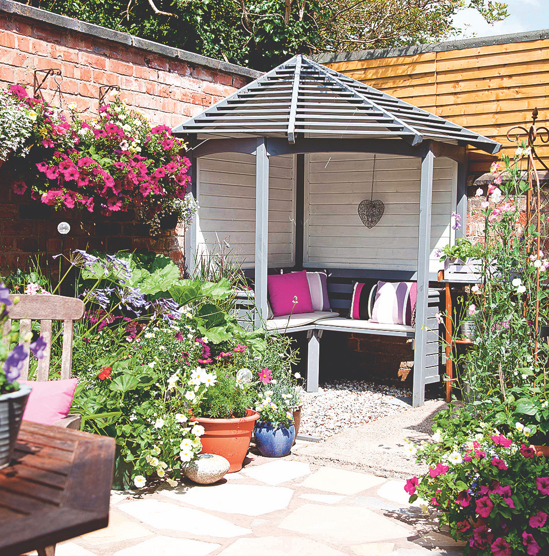 Sheltered seating area in corner of garden surrounded by potted plants