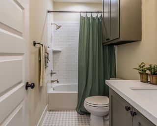 A small beige bathroom with a moss-green shower curtain