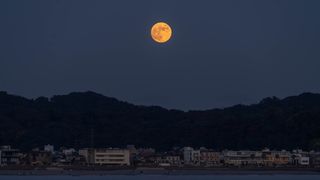 orange hued moon over hills and water below.