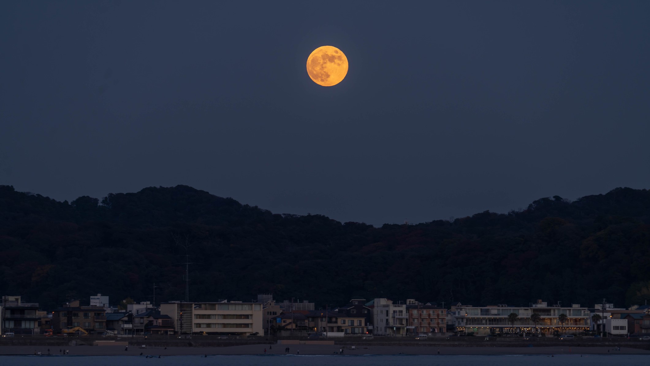 orange hued moon over hills and water below.