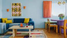Tonal blue denim sofa against light blue wall with orange sconces and yellow artwork