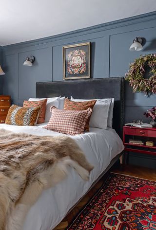 Bedroom with blue panelled walls, leather headboard and red patterned rug