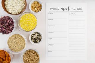 A weekly meal planner next to various foods in bowls.