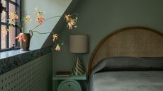 green color-drenched bedroom with green marble windowsill, roman blinds, rattan bedhead, green side table with striped lamp, and green bedding