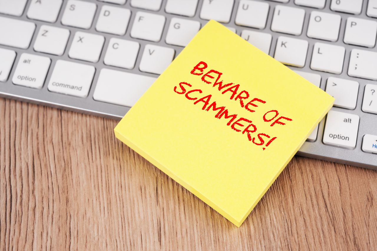 Post it note reading &quot;Beware of Scammers!&quot; on a computer keyboard. 