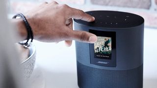 A hand presses buttons on the Bose Home Speaker 500