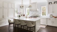 All white kitchen with mahogany hardwood flooring, a large kitchen island with white bar chairs and low pendant lighting