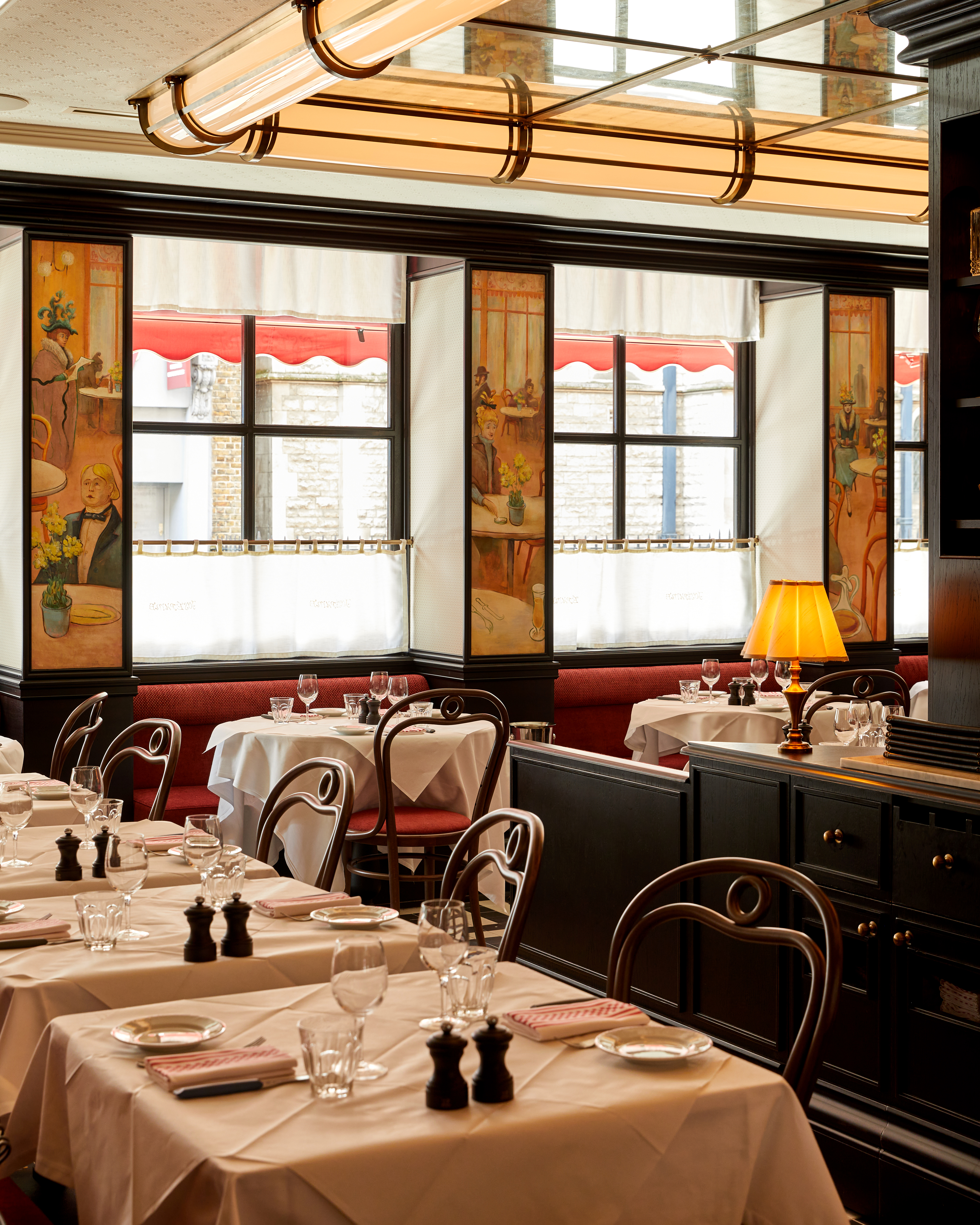 A quirkily decorated modern bistro with reflective ceilings, run-through cylindrical lighting in brass and glass, handpainted murals, cafe-style curtains, old-style table lamps, and Bentwood chairs.