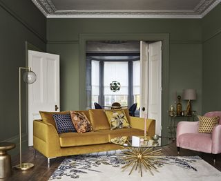 mustard yellow velvet sofa with Aquaclean in green living room, with a white rug, pink armchair, and gold lamp and coffee table
