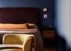 A small bedroom painted dark blue with a gold wall sconce above a wooden nightstand