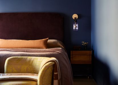 A small bedroom painted dark blue with a gold wall sconce above a wooden nightstand