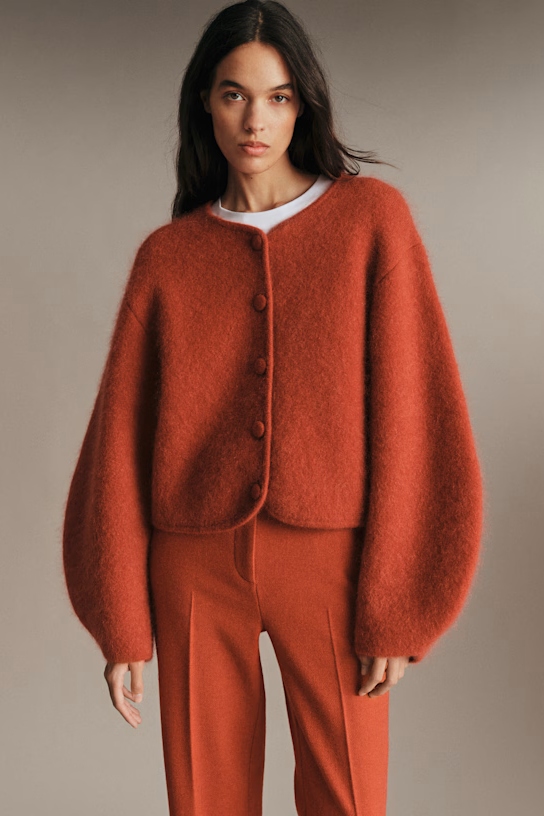 A model wearing an orange-red cardigan.