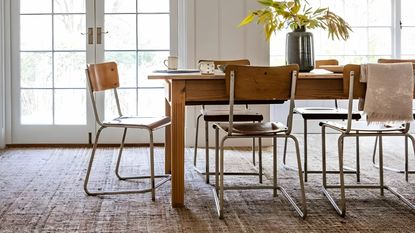 Textured brown carpet in dining room, dark wood dining table, wood and metal dining chairs, low hanging pendant lights, flowers on table