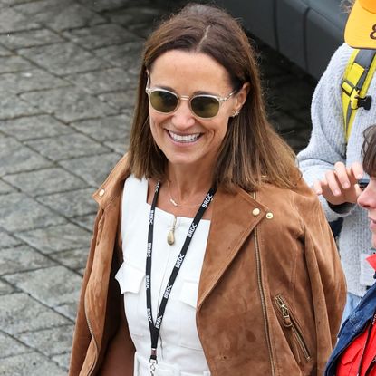 Pippa Middleton wearing a suede jacket and white dress walking outside at British Grand Prix