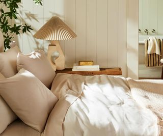 Side view of Brooklinen Luxe Sateen Sheet Set on a bed against a cream wall.