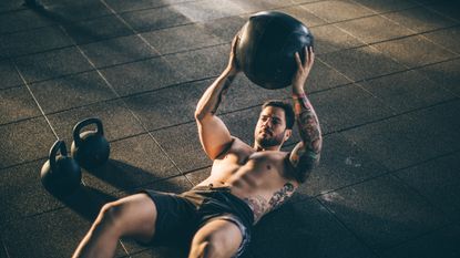 Man doing a sit up in the gym with a slam ball