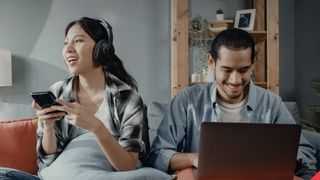 A woman listening to music on a smartphone and a man using a laptop