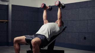 Man performing hammer press with dumbbells on a weights bench set at an incline