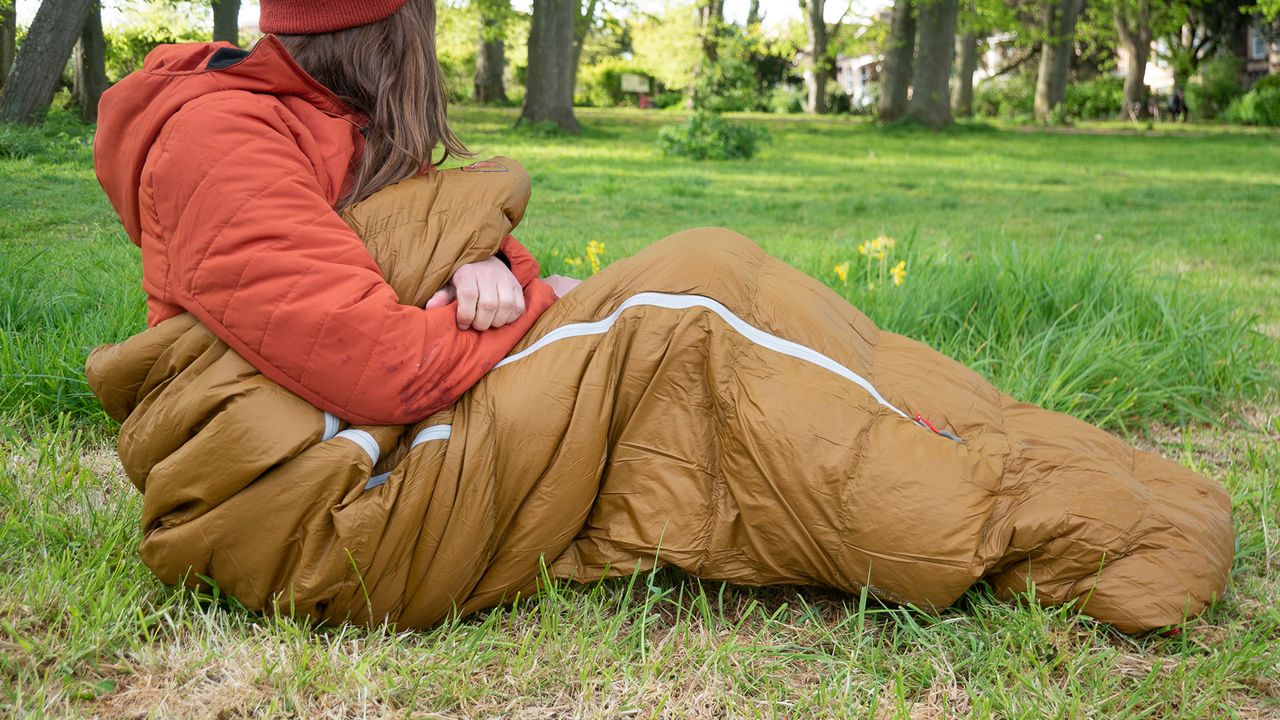 Woman sitting inside Robens Icefall Pro 300 sleeping bag on some grass