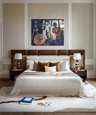 neutral bedroom with bed with oversized leather headboard, colorful statement artwork and neutral patterned rug
