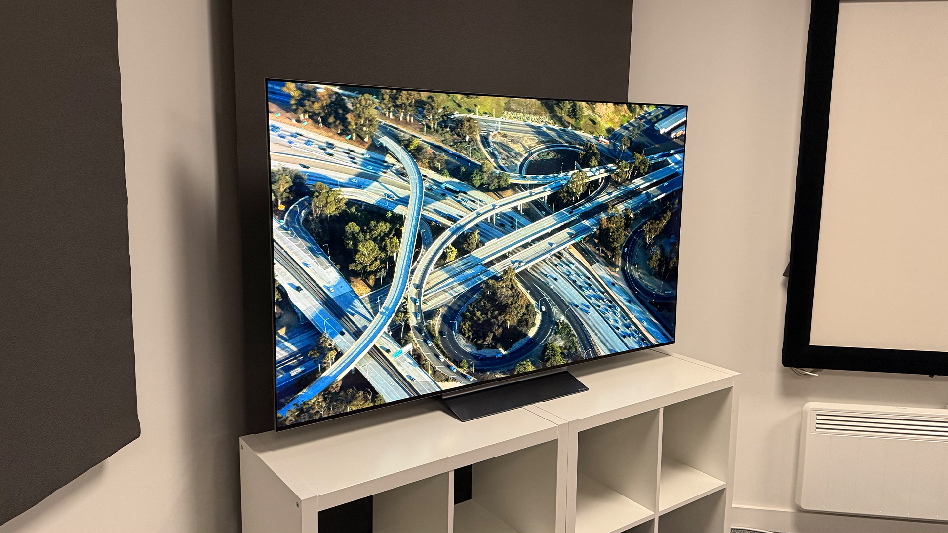 LG C6 OLED TV on white shelving unit, on screen is aerial view of road junctions