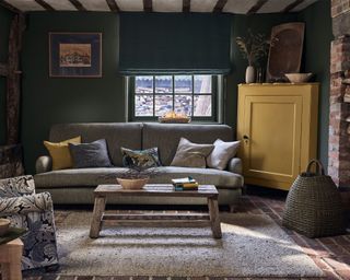 Dark green painted living room with yellow painted furniture, grey sofa, william morris print lounge chair and cushions, dark wooden features