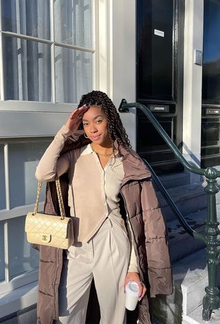 a roundup of the best puffer jackets shown in a photo of a woman wearing a brown puffer coat over a tan blazer with yellow trousers and black boots