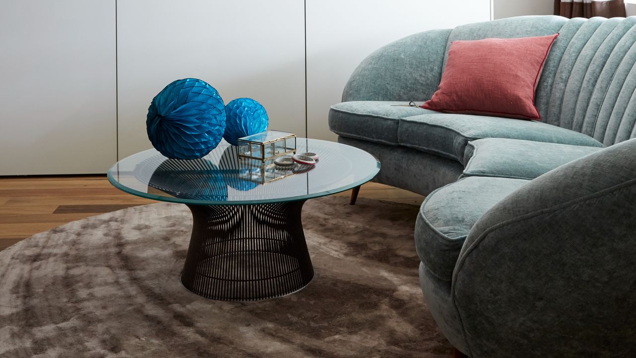 A living room with a curved light blue sofa and a round glass coffee table on a round rug