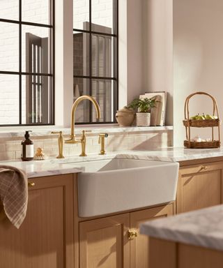 A kitchen with wooden cabinetry, a deep white sink and gold hardware