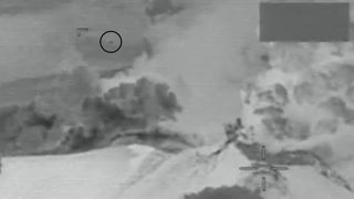 a blurry black dot flying above a snow-covered volcano in grainy black-and-white footage