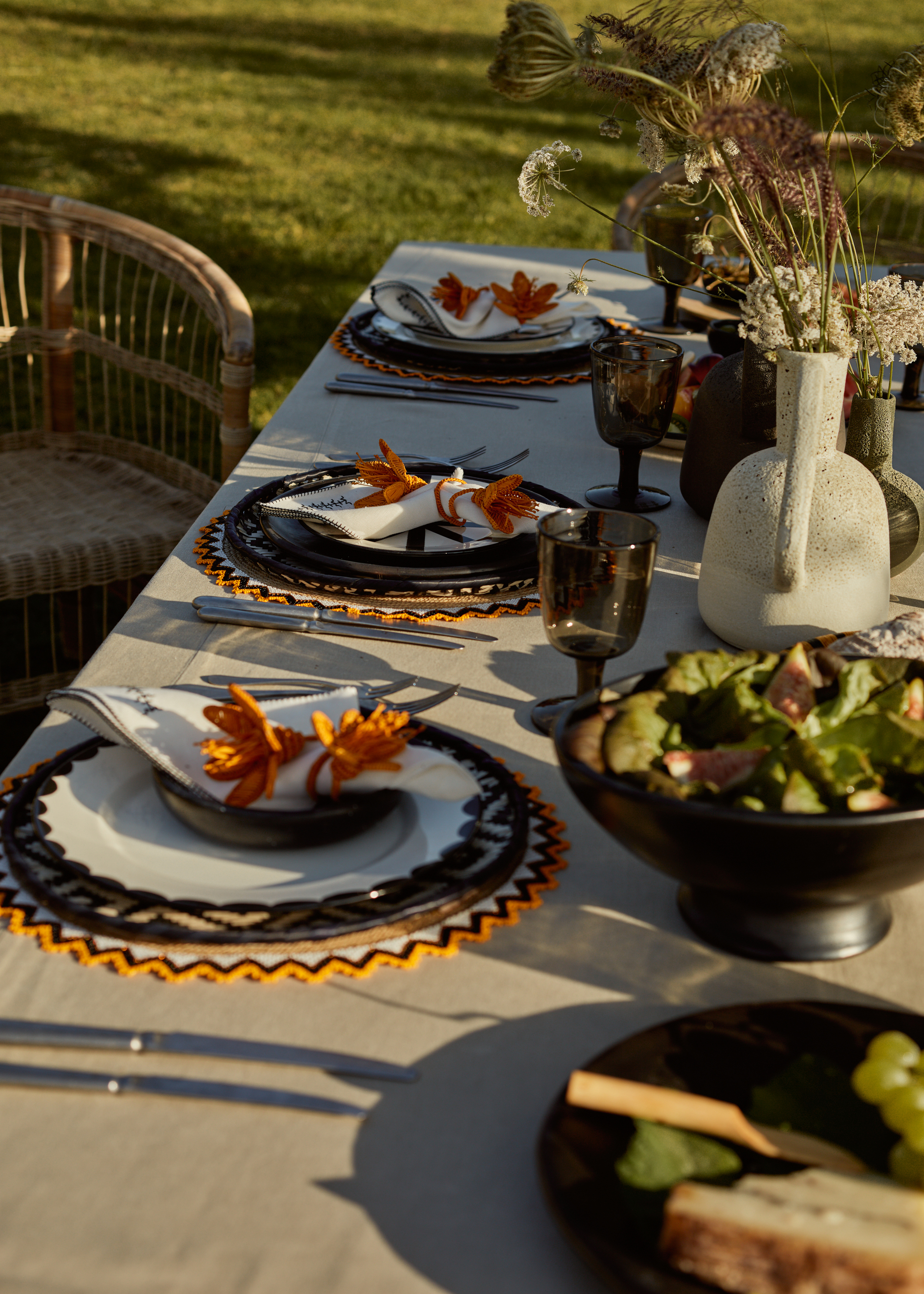 An outdoor table set for dinner with placemats, bowls, and floral napkin rings