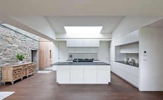 Contemporary white kitchen with rooflight and stone walls