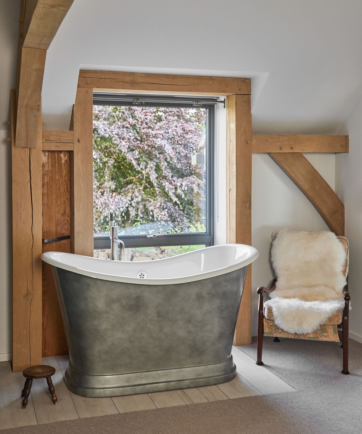 A metal freestanding bathtub in front of a window with lots of exposed beams