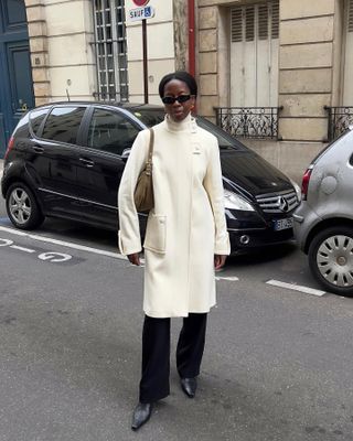 Woman wearing cream-colored coat and black flared pants on a Parisian-style street