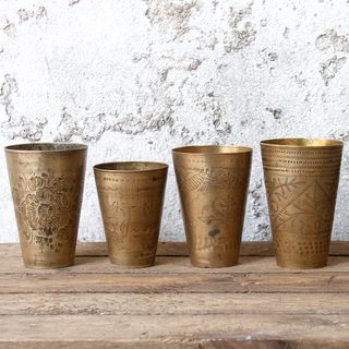 four brass cups kept on wooden table