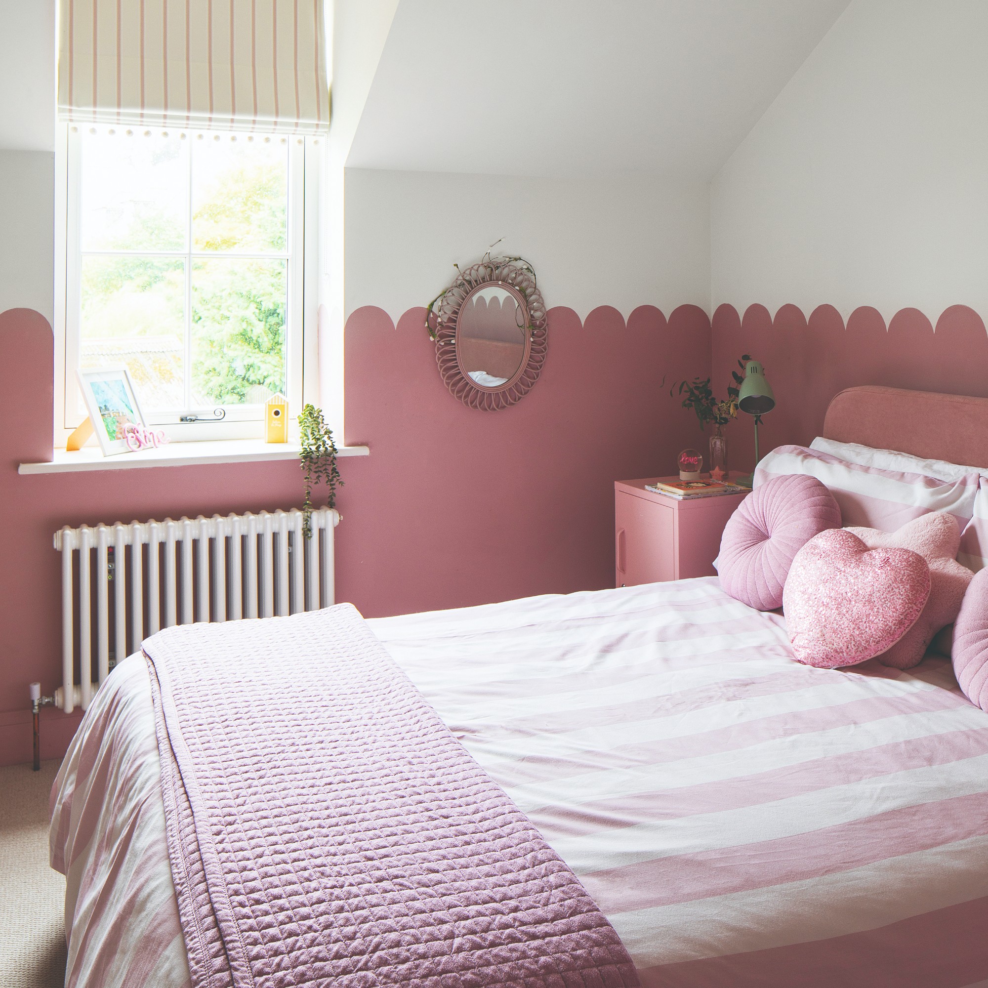 A bedroom with two-toned walls in white and pink separated by a scalloped edge with pink and white striped bed linen on the bed