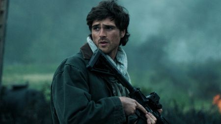 Jacob Elordi's Hig looking over his right shoulder and holding a gun in The Dog Stars