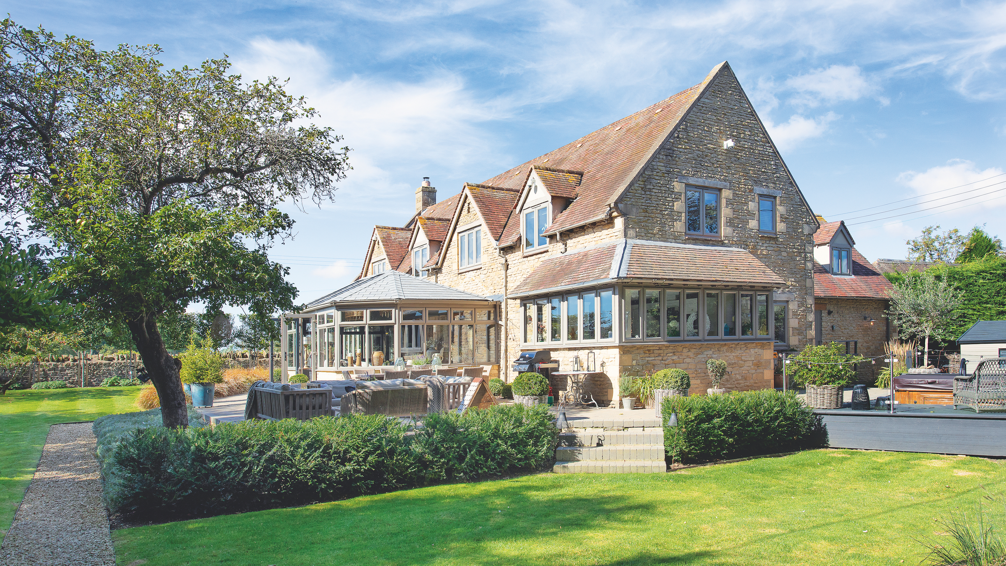 exterior of large cotswold stone house with garden room and large green lawn