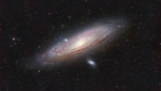 A large spiral galaxy is pictured shining against a colorful starfield.
