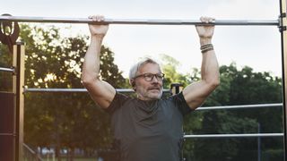 A middle aged man, in great physical shape, performs an upper body workout in a park