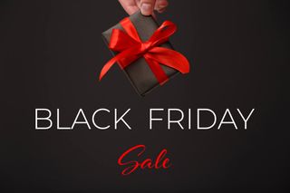 Black Friday Sale. Woman's hand holding black gift box with red bow over black background.