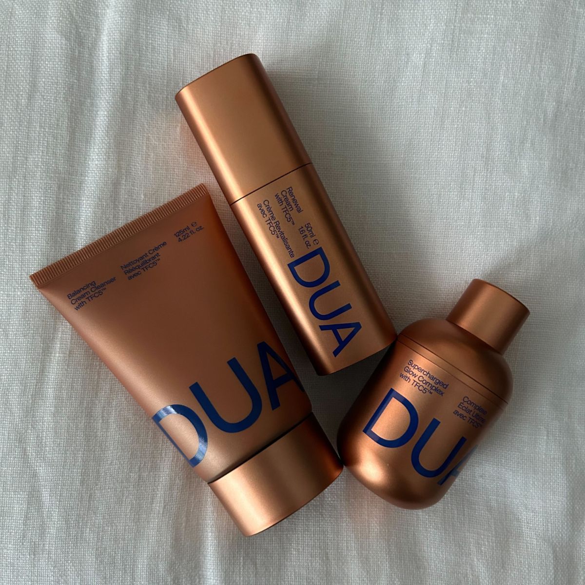 Dua Lipa x Augustinus Bader skincare products on a white linen background