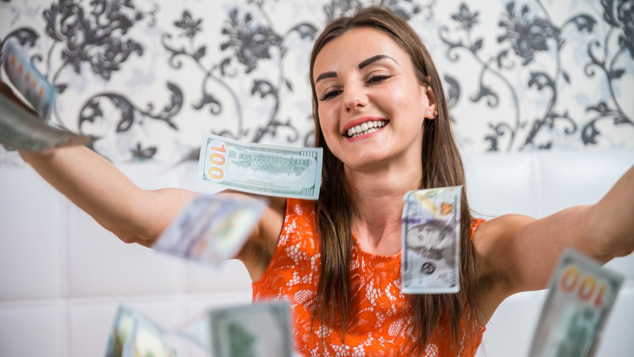 A young woman throws hundred-dollar bills into the air.