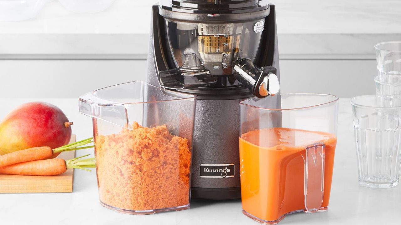 The gray Kuvings EVO820 juicer making mango and carrot juice. There is a collection of orange-colored juicer on one side and the waste on the other