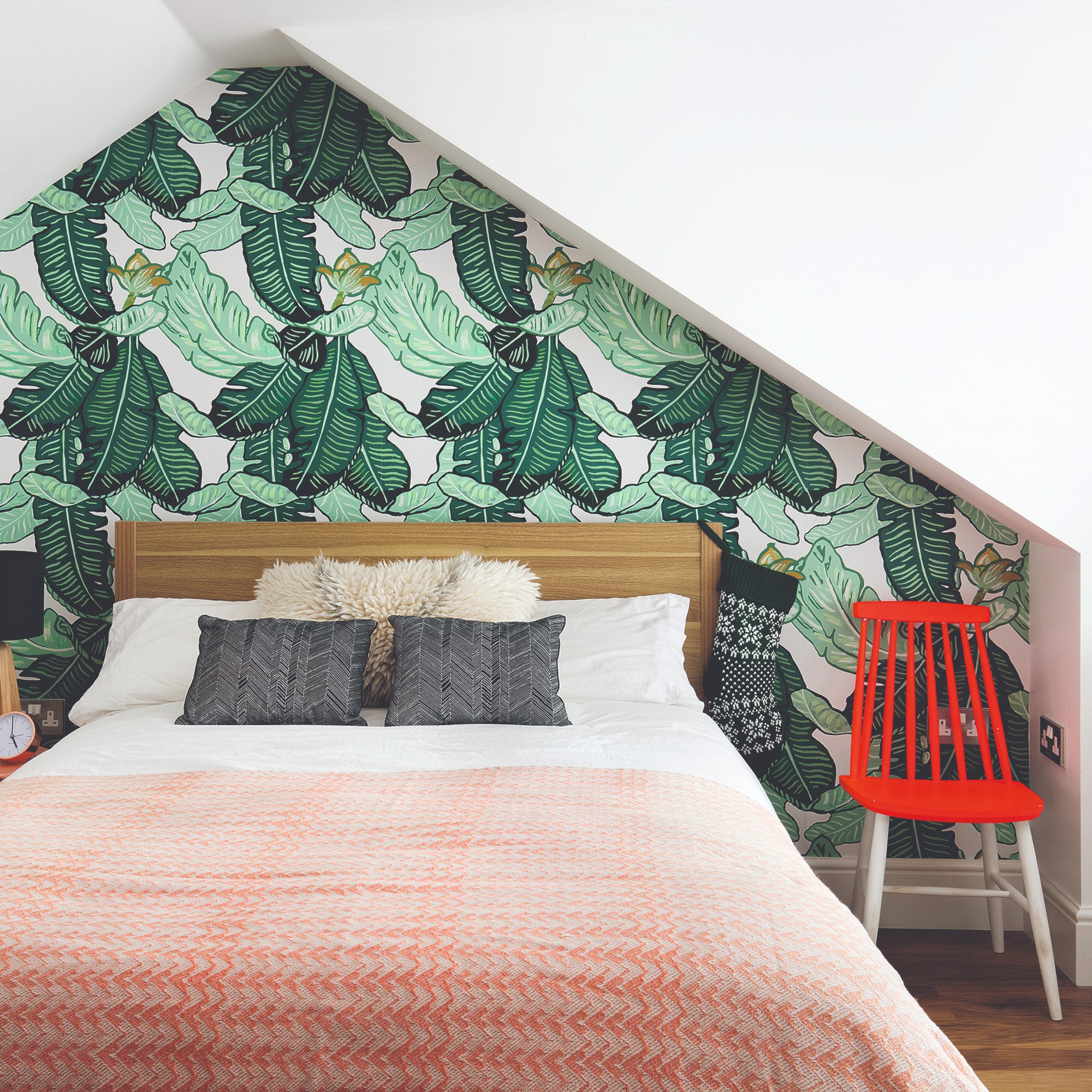 A bedroom with an alcove surrounding the headboard covered in a palm leaf-print wallpaper