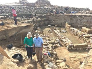 Researchers stand near the ruins of ancient walls, with the destruction layer about midway down each exposed wall.